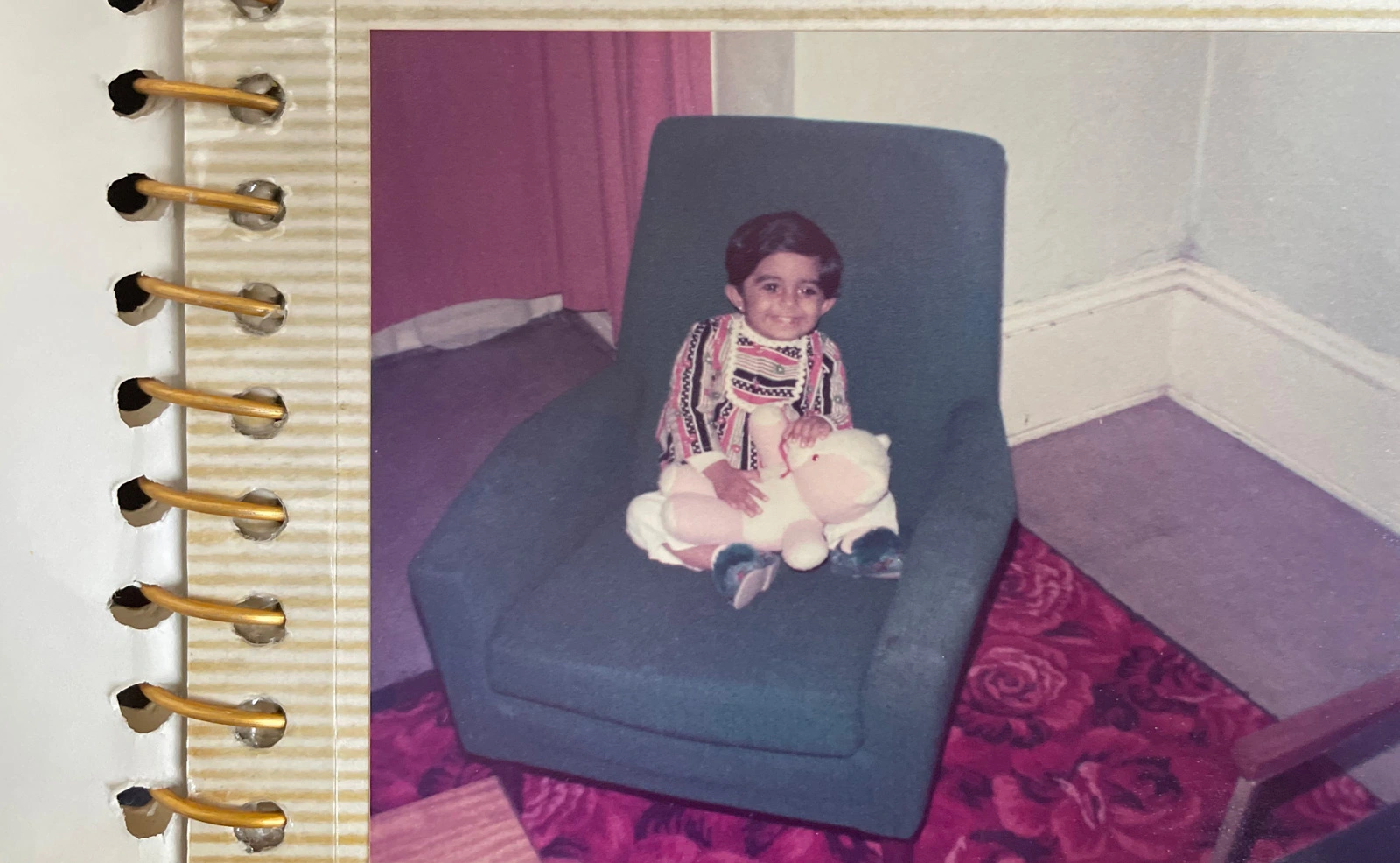 Image of a young happy child holding a teddy bear sat on a blue sofa